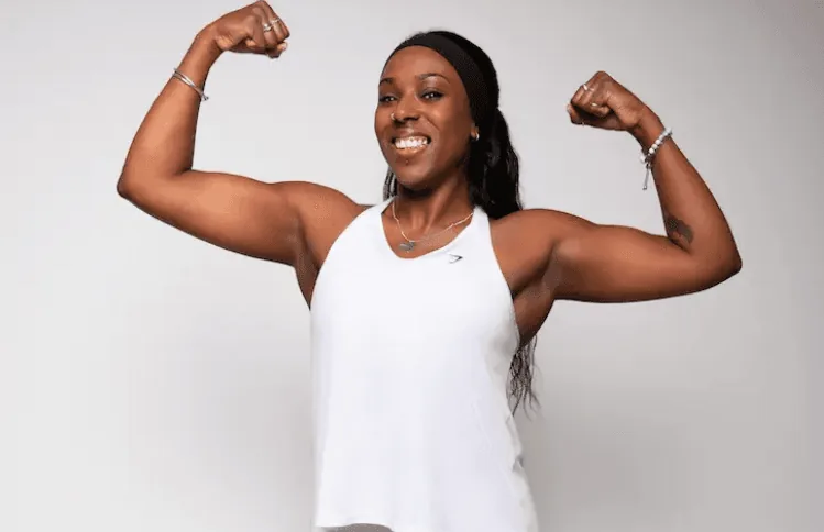 Faye flexing both arms and grinning in a white vest