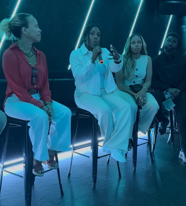Faye speaking on a panel, seated on a high stool under blue stage lights