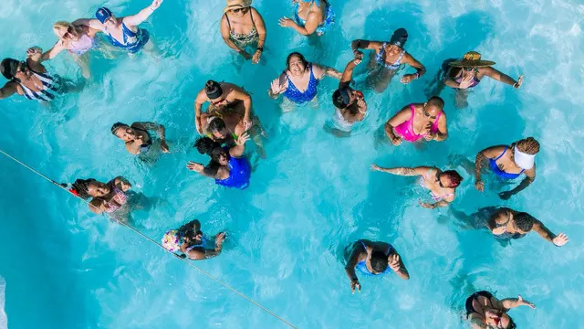 A retreat group laughing together in a turquoise pool, seen from above